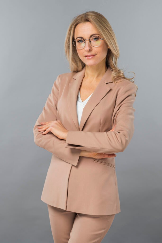 confident-young-businesswoman-standing-with-her-arm-crossed-against-gray-backdrop